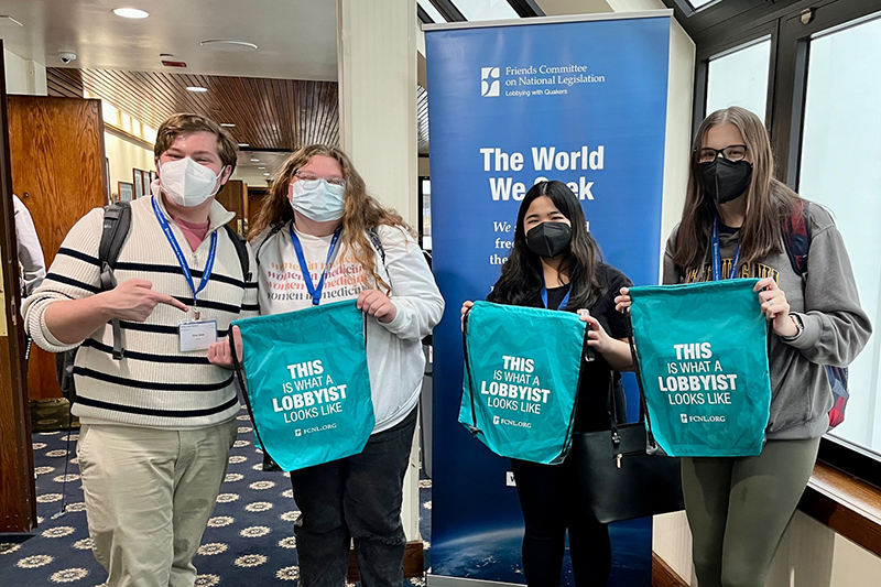 Four students standing in a hallway hold up drawstring bags reading "This is what a lobbyist looks like"