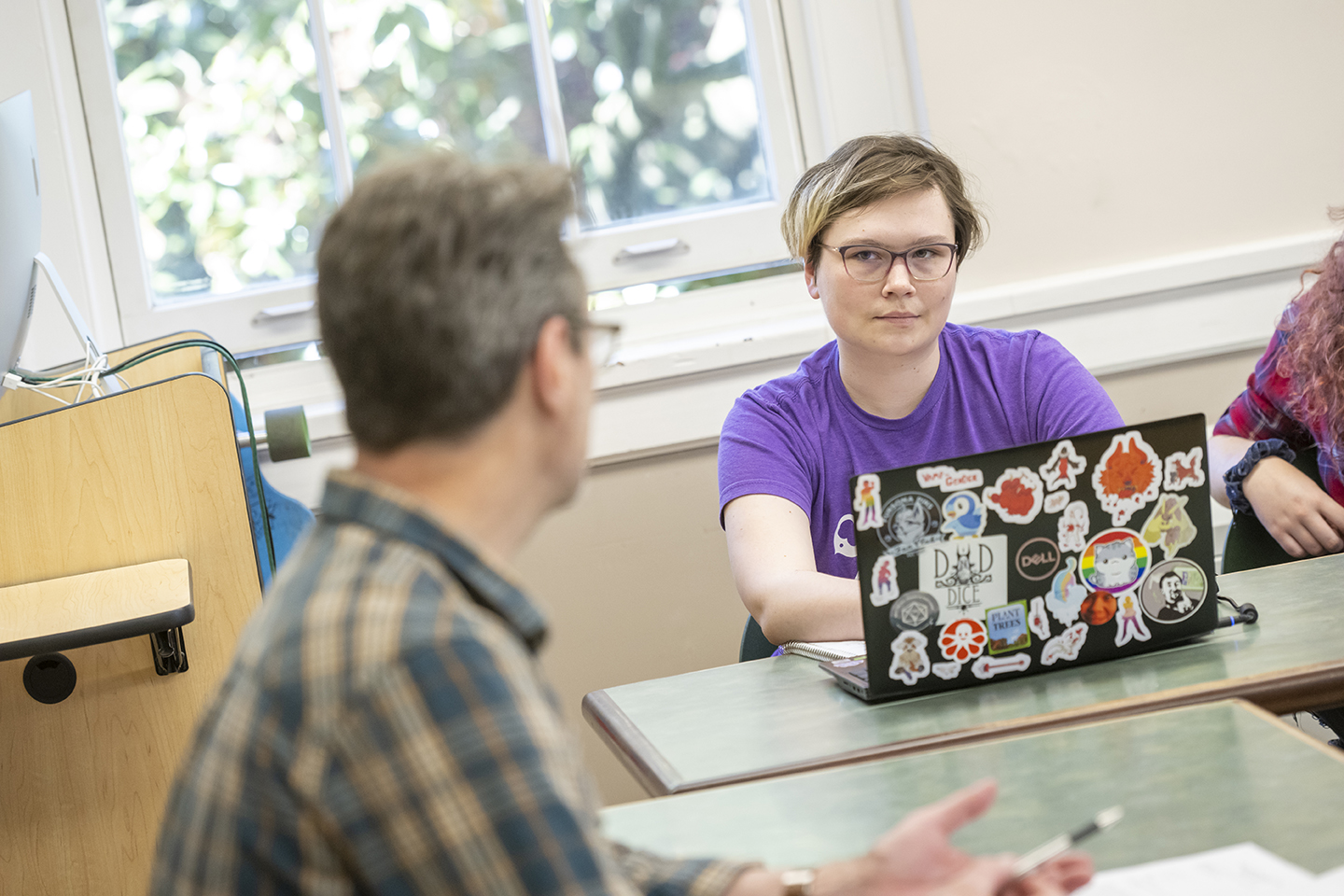 student writing on laptop listens to professor