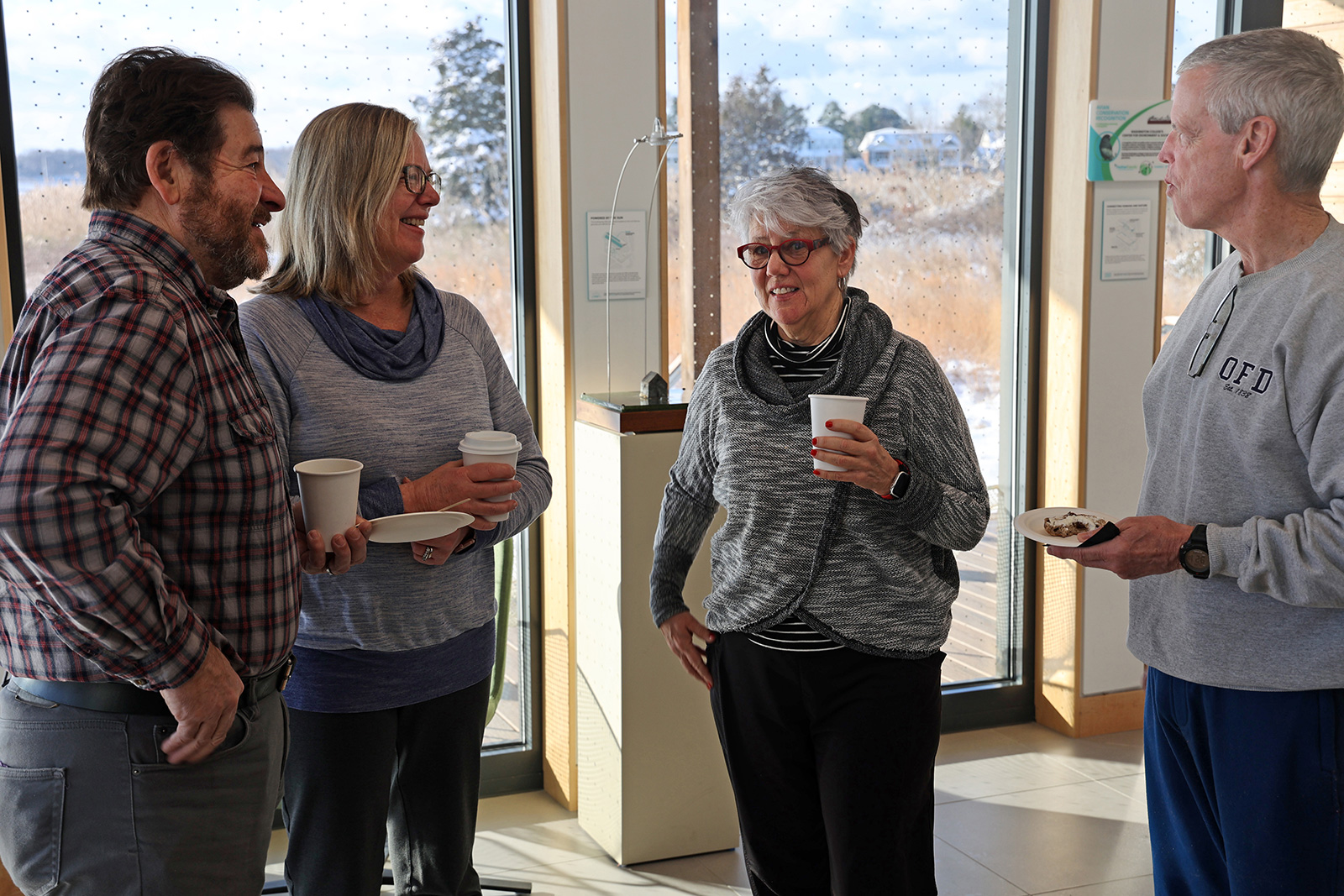 Four people standing, chatting, and drinking coffee