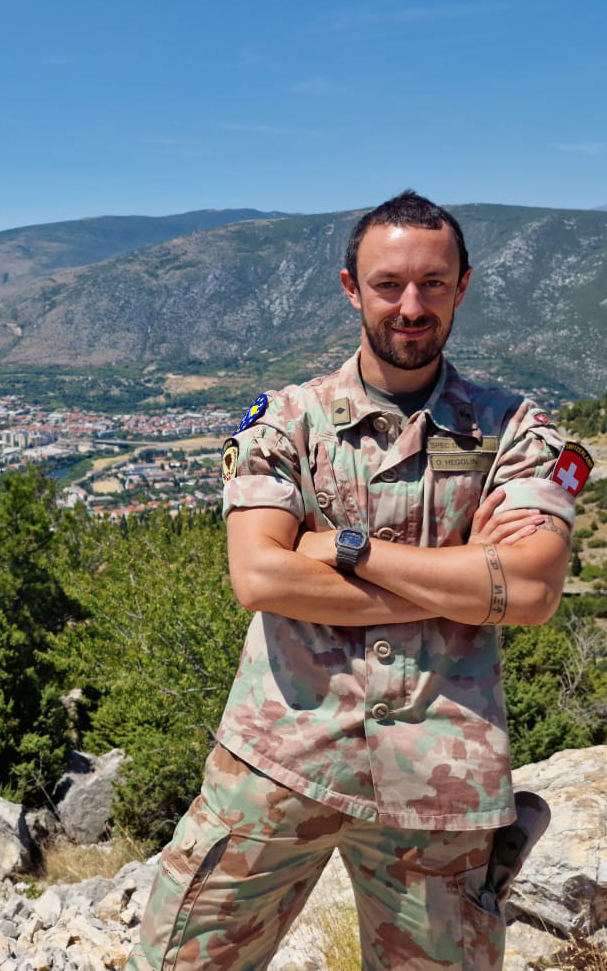 Oliver Hegglin in uniform on a hilltop with a town in the valley behind him